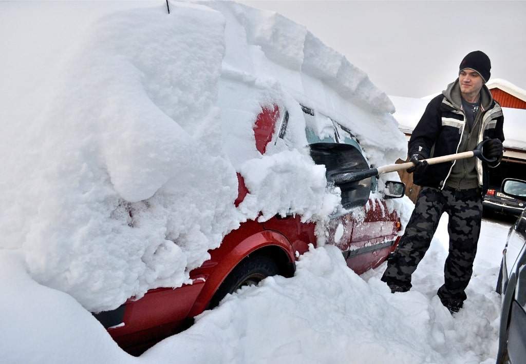 A man removing the snow off his vehicle after a blizzard.