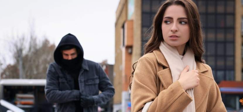 Person looking cautiously over their shoulder while walking down a street.